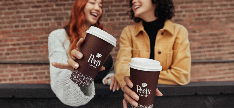 Two women laughing and talking while holding Peet's Coffee cups